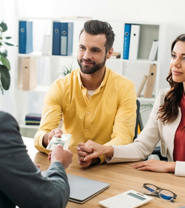couple investors sitting at table and taking dollar banknotes from advisor in office e1715620952323 couple investors sitting at table and taking dollar banknotes from advisor in office e1715620952323